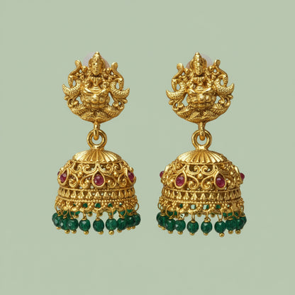Gold earrings with green and red gemstones on a light green background