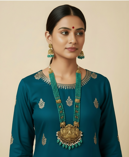 Woman wearing a teal traditional outfit with gold jewelry on a beige background