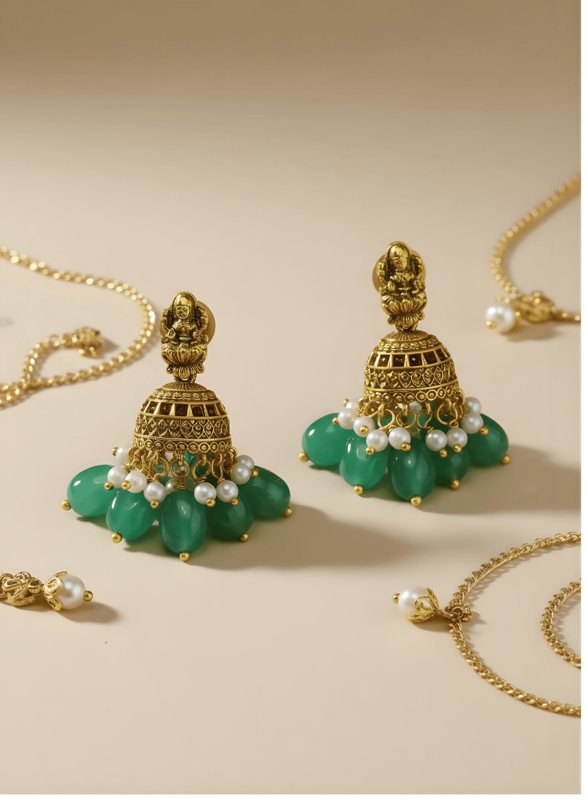 Gold and green earrings with pearl accents on a beige background