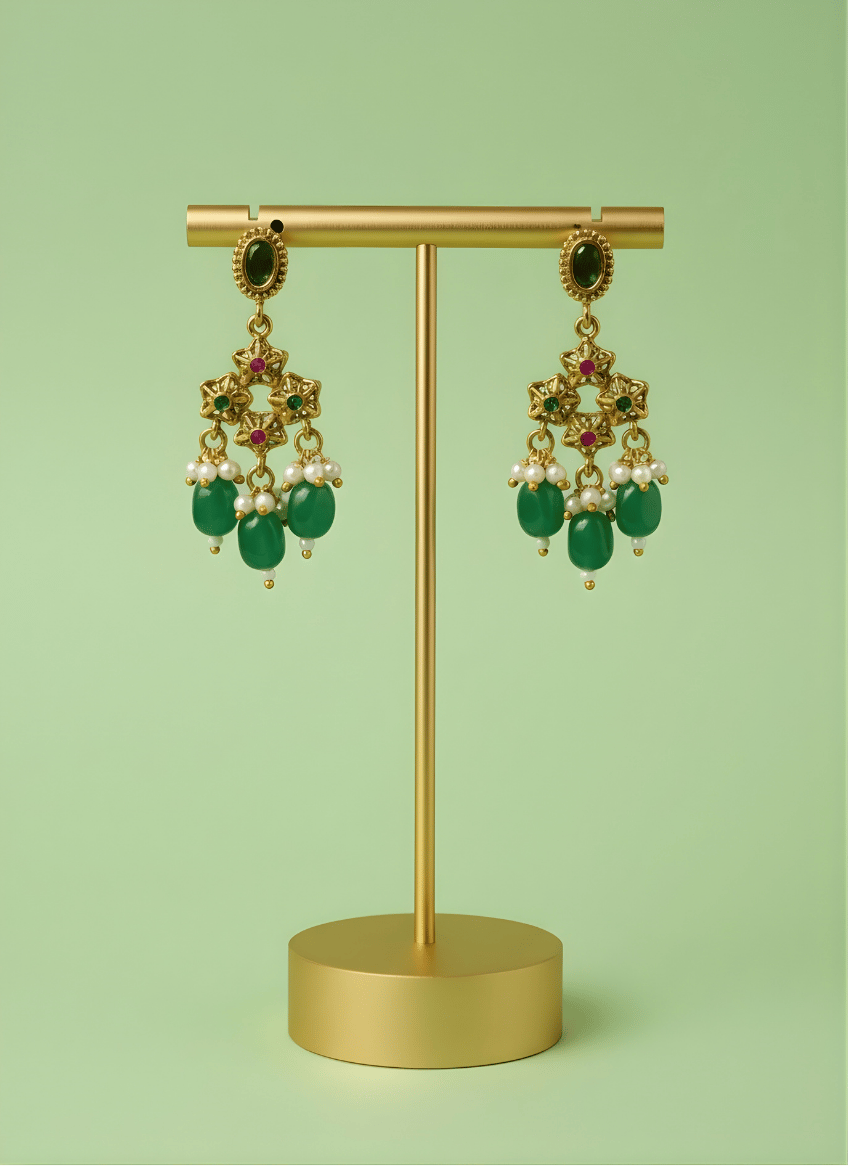 Gold earrings with green beads and pearls on a gold stand against a light green background