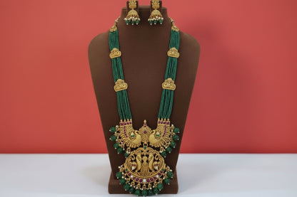 Ornate gold and green beaded necklace with matching earrings on a light pink background