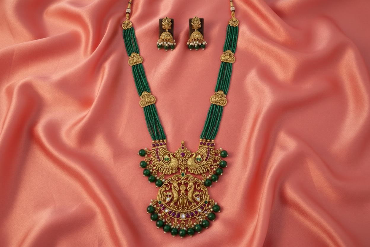 Ornate green and gold necklace with matching earrings on a pink fabric background