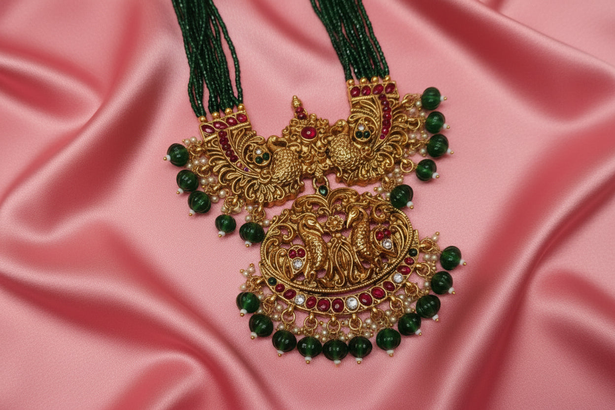 Ornate gold necklace with green beads on a light pink background