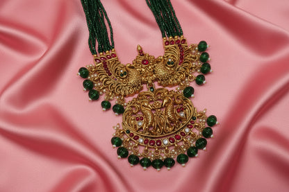 Ornate gold necklace with green beads on a light pink background
