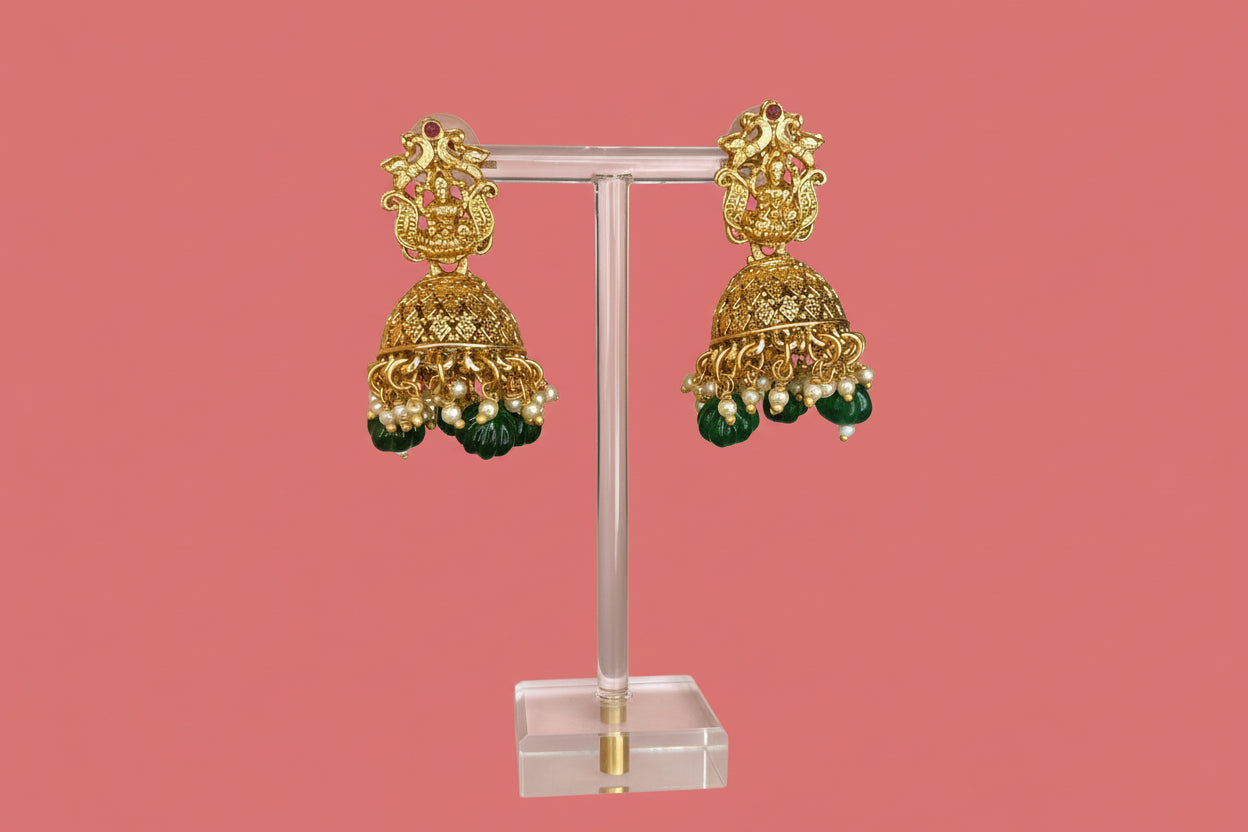 Gold and green earrings on a stand with a pink background