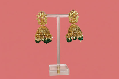 Gold and green earrings on a stand with a pink background