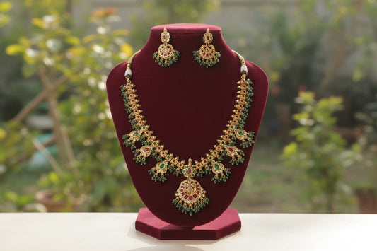 Gold necklace with green and red stones on a red stand