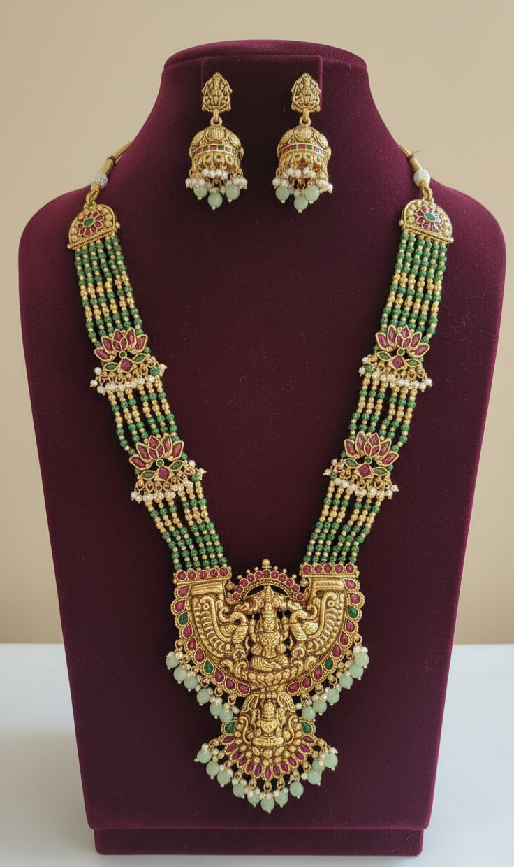 Gold necklace with green and red stones on a white background