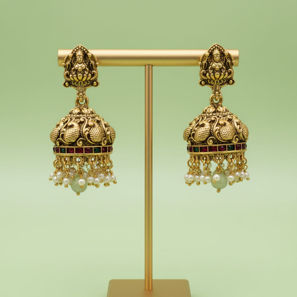 Gold earrings with intricate designs and pearl-like beads on a green background