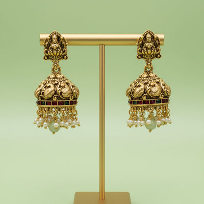 Gold earrings with intricate designs and pearl-like beads on a green background