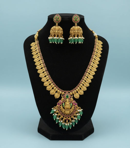 Gold necklace and earrings set on a black stand with a gray background