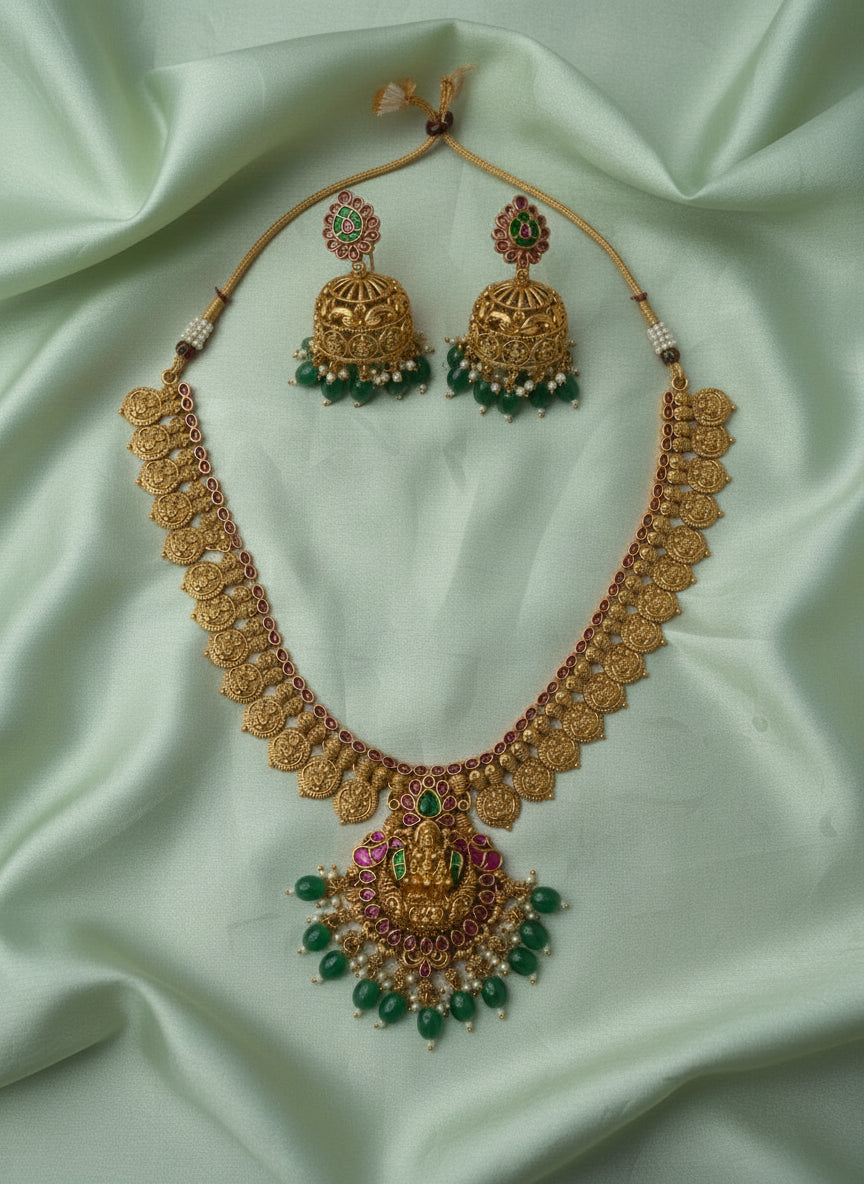 Gold necklace with green beads and matching earrings on a gray background