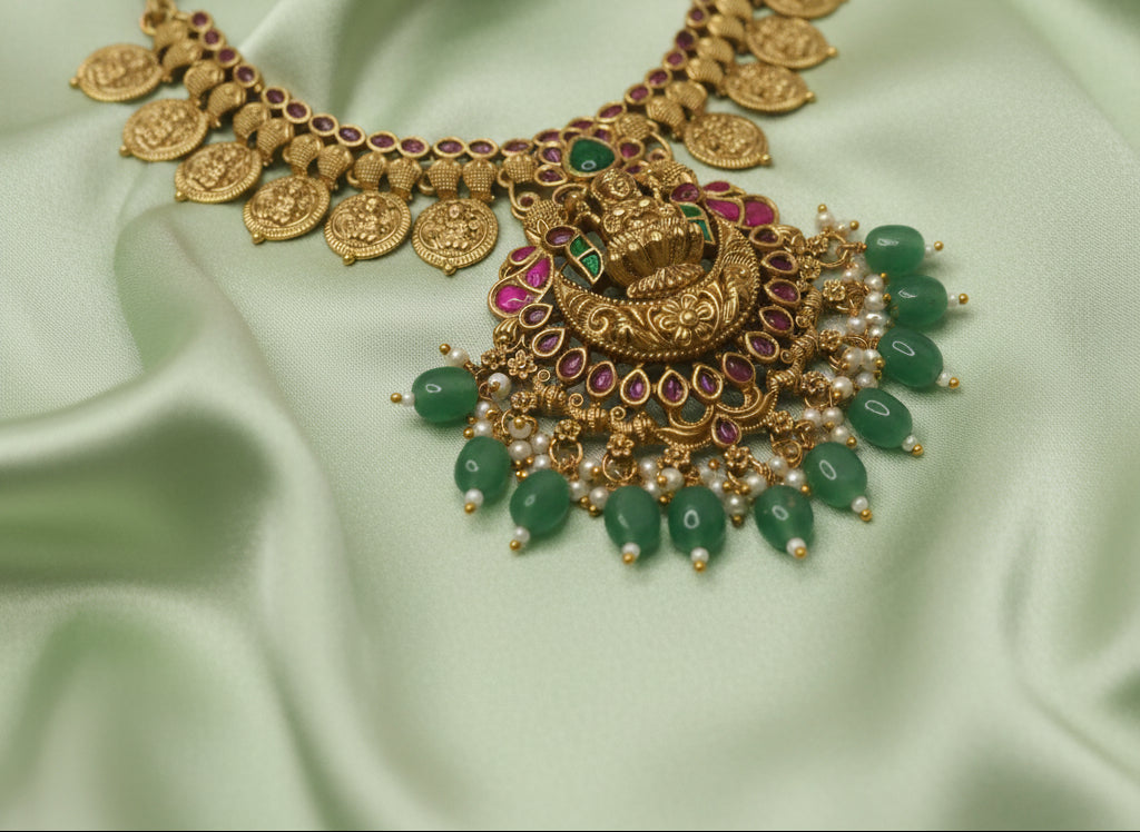 Ornate gold necklace with green stones on a light fabric background