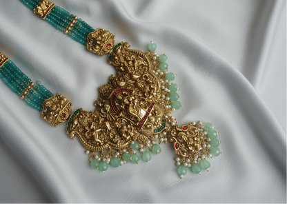 Ornate gold and green beaded south indian necklace with matching earrings on a light green fabric background