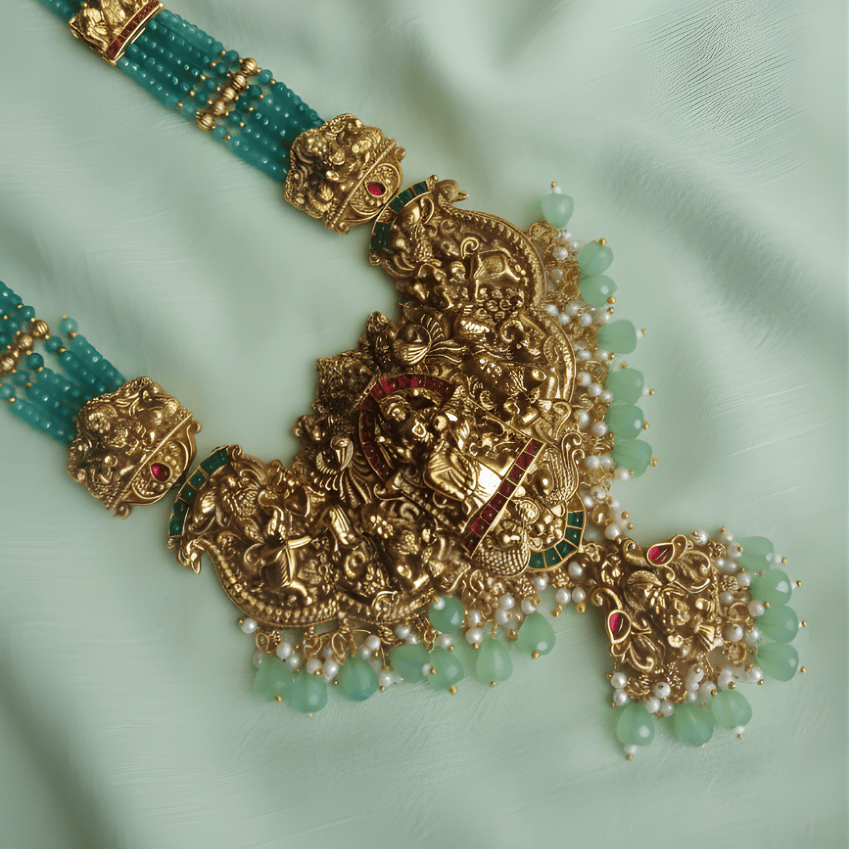 Ornate gold and green beaded south indian necklace with matching earrings on a light green fabric background