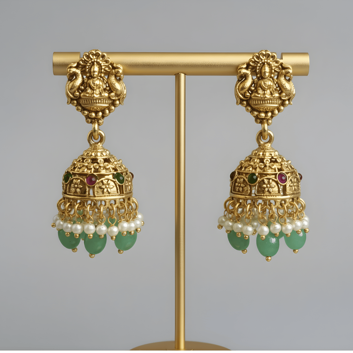 Gold south earrings with green and pearl accents on a gold stand against a gray background