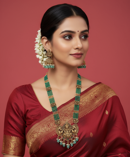 Woman wearing a red saree with gold border and green jewelry against a red background