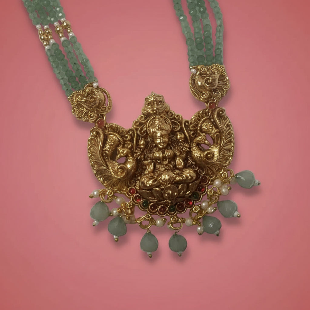 Gold necklace with intricate design and green beads on a pink background