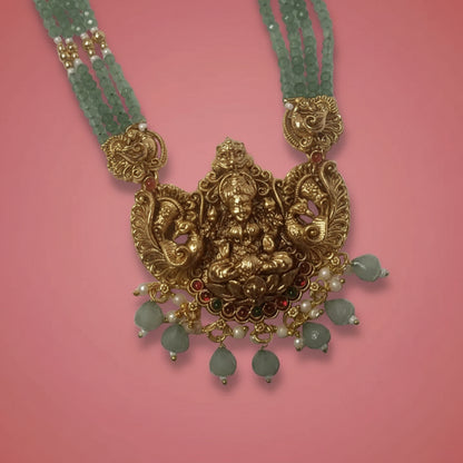 Gold necklace with intricate design and green beads on a pink background
