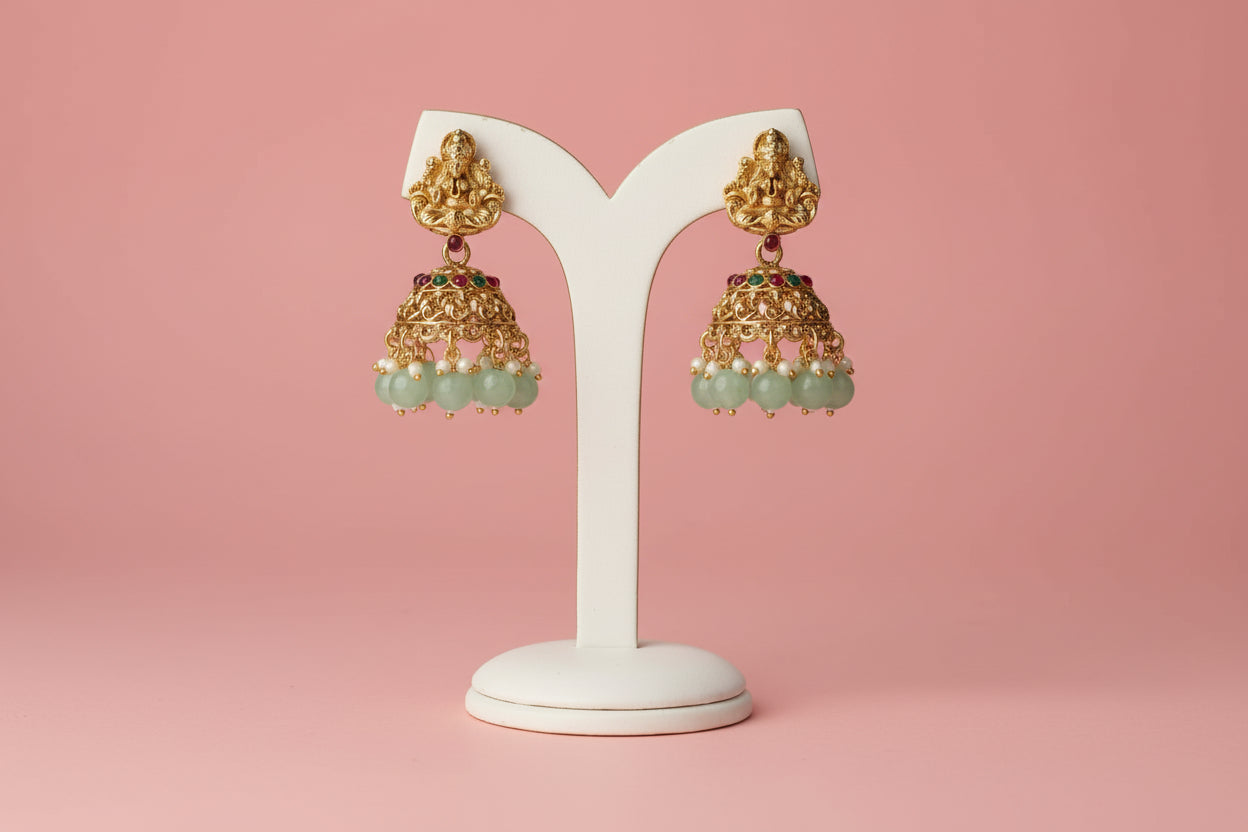 Gold earrings with green beads held in a hand against a colorful book background