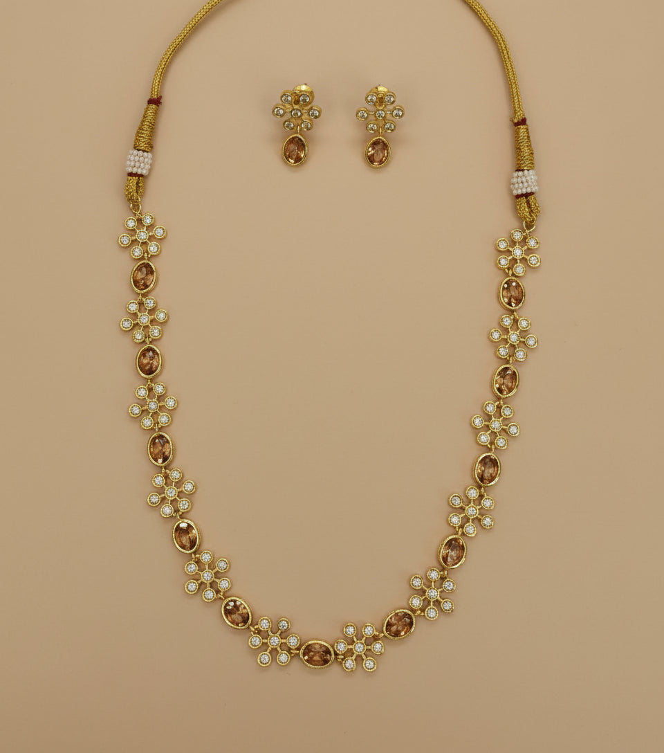 Gold necklace with floral designs and matching earrings on a white background