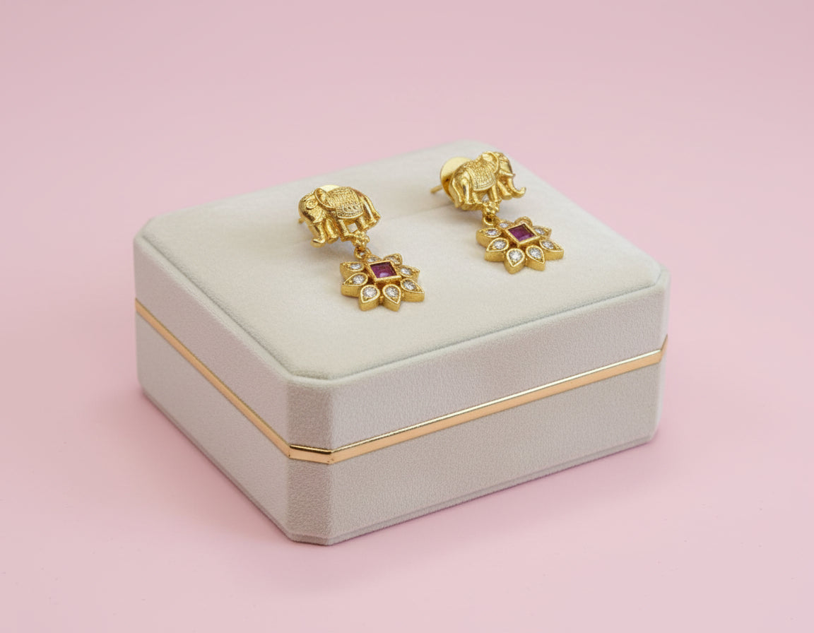 Gold earrings with red gemstones on a light gray jewelry box against a pink background