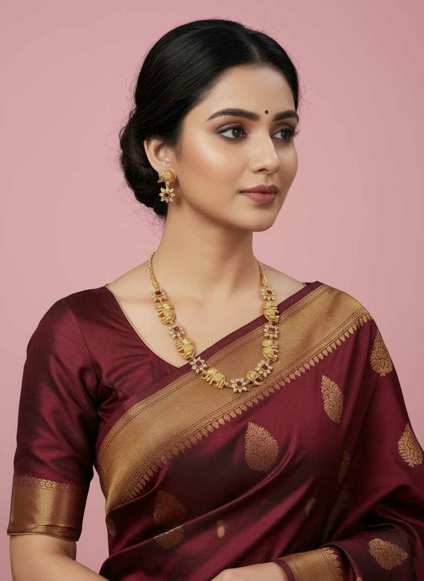 Woman wearing a maroon saree with gold border and jewelry on a gray background
