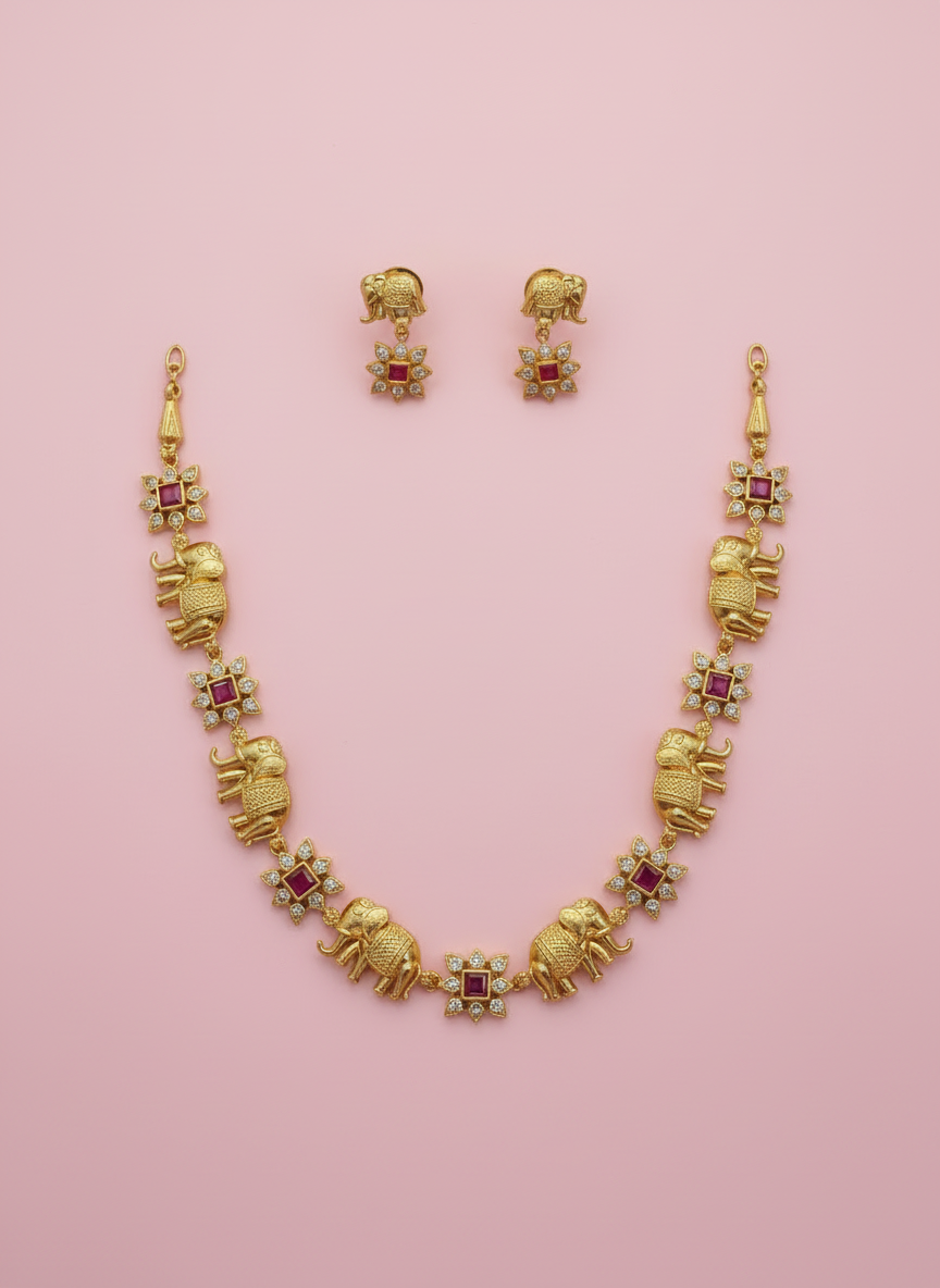 Gold necklace with elephant design and red stones on a pink background