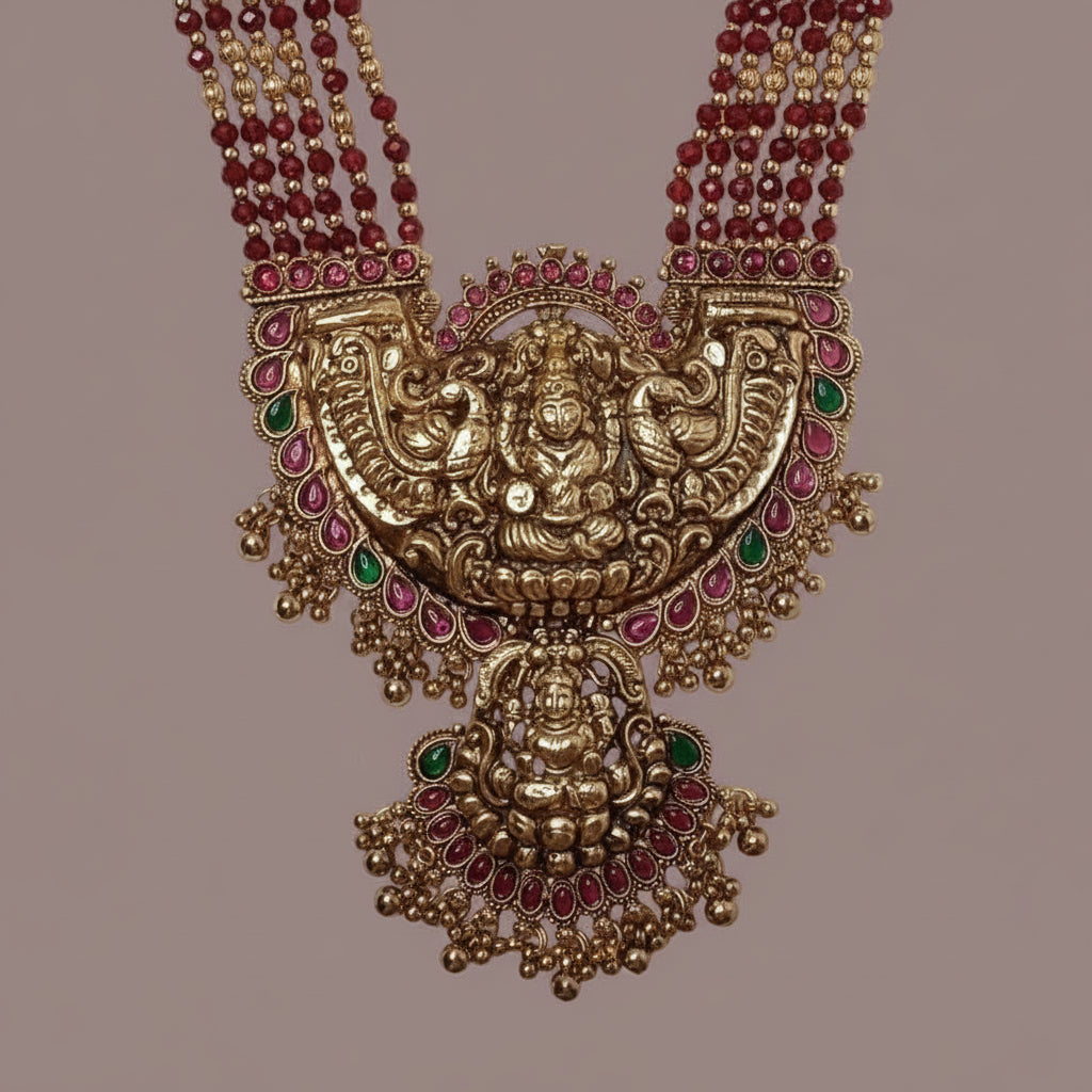 Ornate gold necklace with red and green gemstones on a beige background