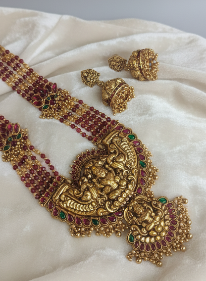 Gold necklace with red and green stones on a white fabric background
