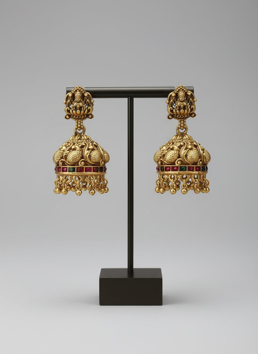 Gold earrings with intricate designs on a black stand against a gray background