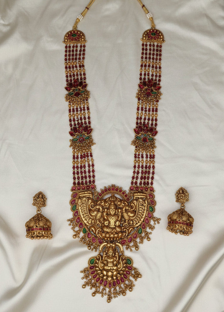 Ornate gold necklace with red beads and matching earrings on a white fabric background