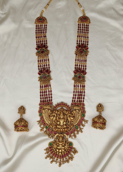 Ornate gold necklace with red beads and matching earrings on a white fabric background