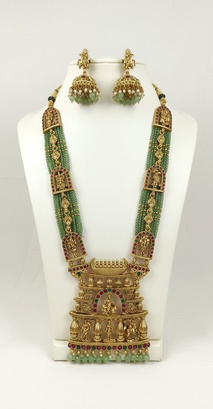 Gold necklace with green beads and matching earrings on a white stand