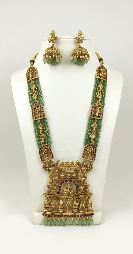 Gold necklace with green beads and matching earrings on a white stand