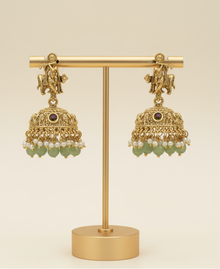 Gold earrings with green stones on a gold stand against a beige background
