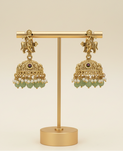 Gold earrings with green stones on a gold stand against a beige background