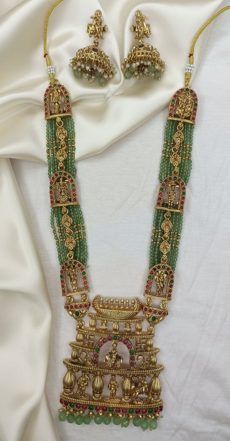 Ornate gold necklace with green beads on a white fabric background