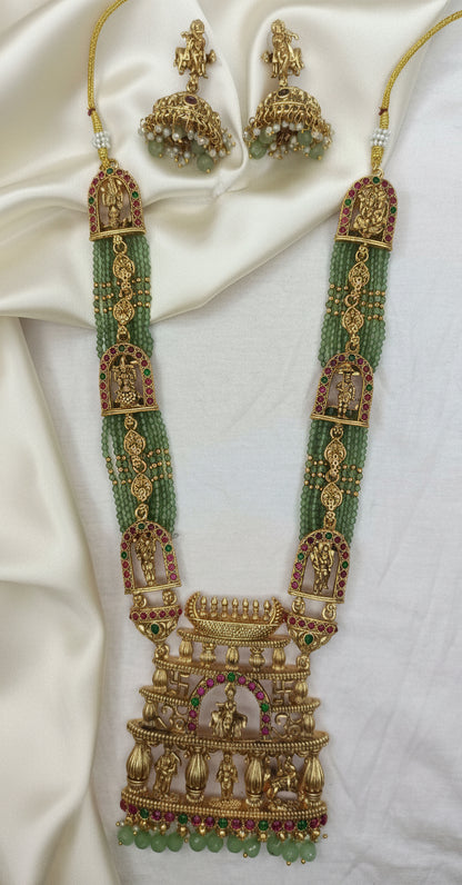 Ornate gold necklace with green beads on a white fabric background