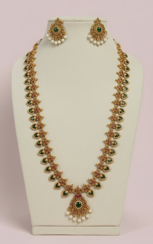 Gold necklace with green gemstones and pearl earrings on a white stand.