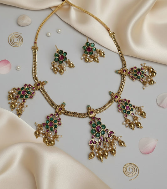 Gold necklace with green and red gemstones on a satin surface