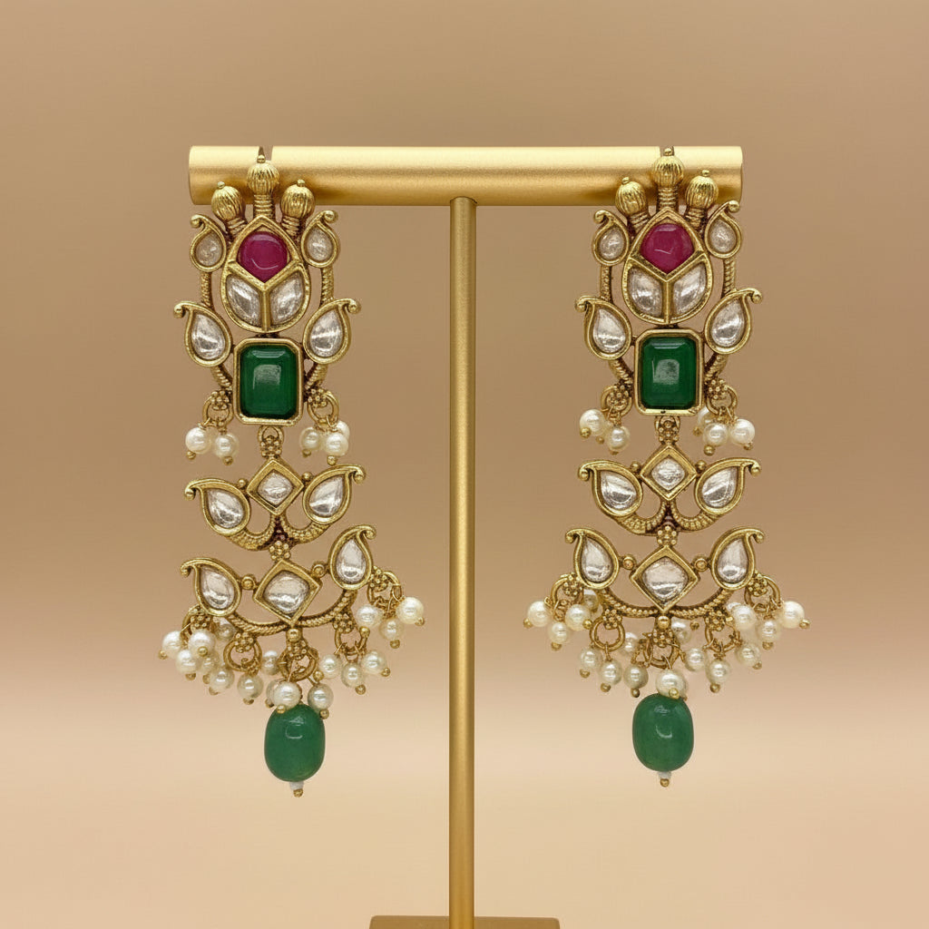 Ornate gold earrings with green and red gemstones on a brown background