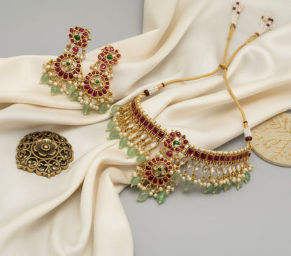 Ornate gold necklace with red and green gemstones on a beige fabric background