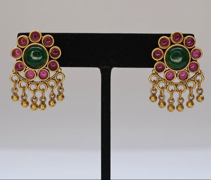 Pair of gold earrings with pink and green gemstones on a black stand against a white background