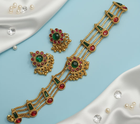 Gold jewelry with green and red stones on a hand