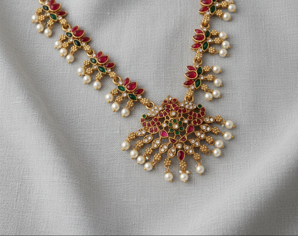 Ornate necklace with pearls, red and green stones on a gray fabric background
