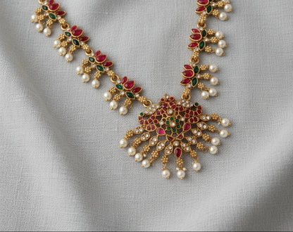 Ornate necklace with pearls, red and green stones on a gray fabric background