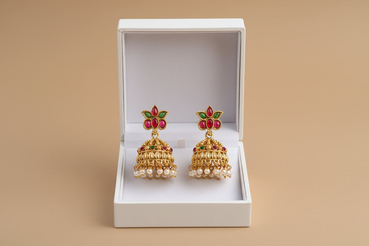 Gold earrings with red and green accents in a white box on a beige background