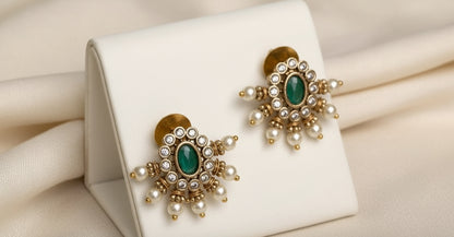 Pair of gold and pearl earrings with green stones on a white cushion
