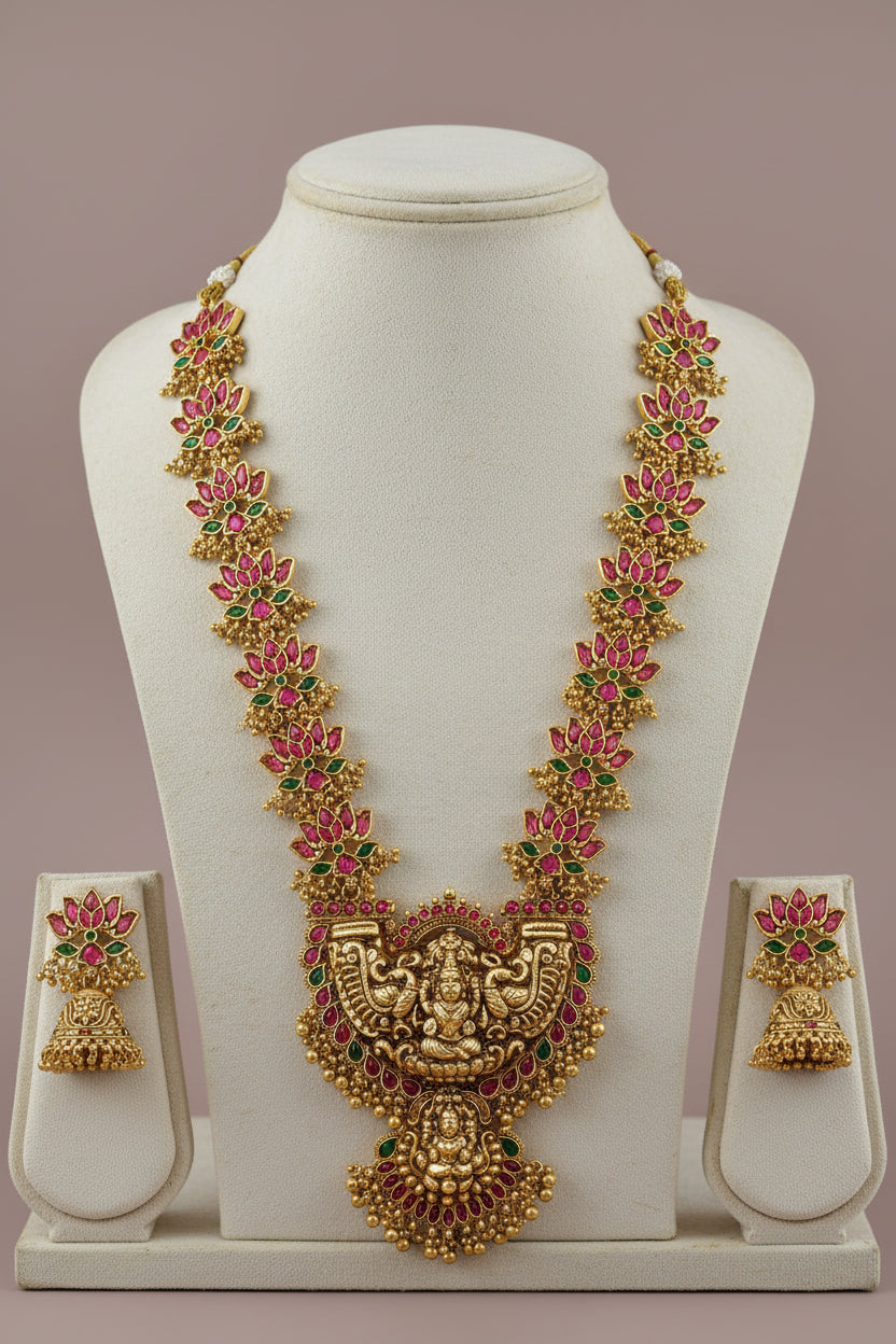 Gold necklace with pink and green stones on a white stand against a beige background